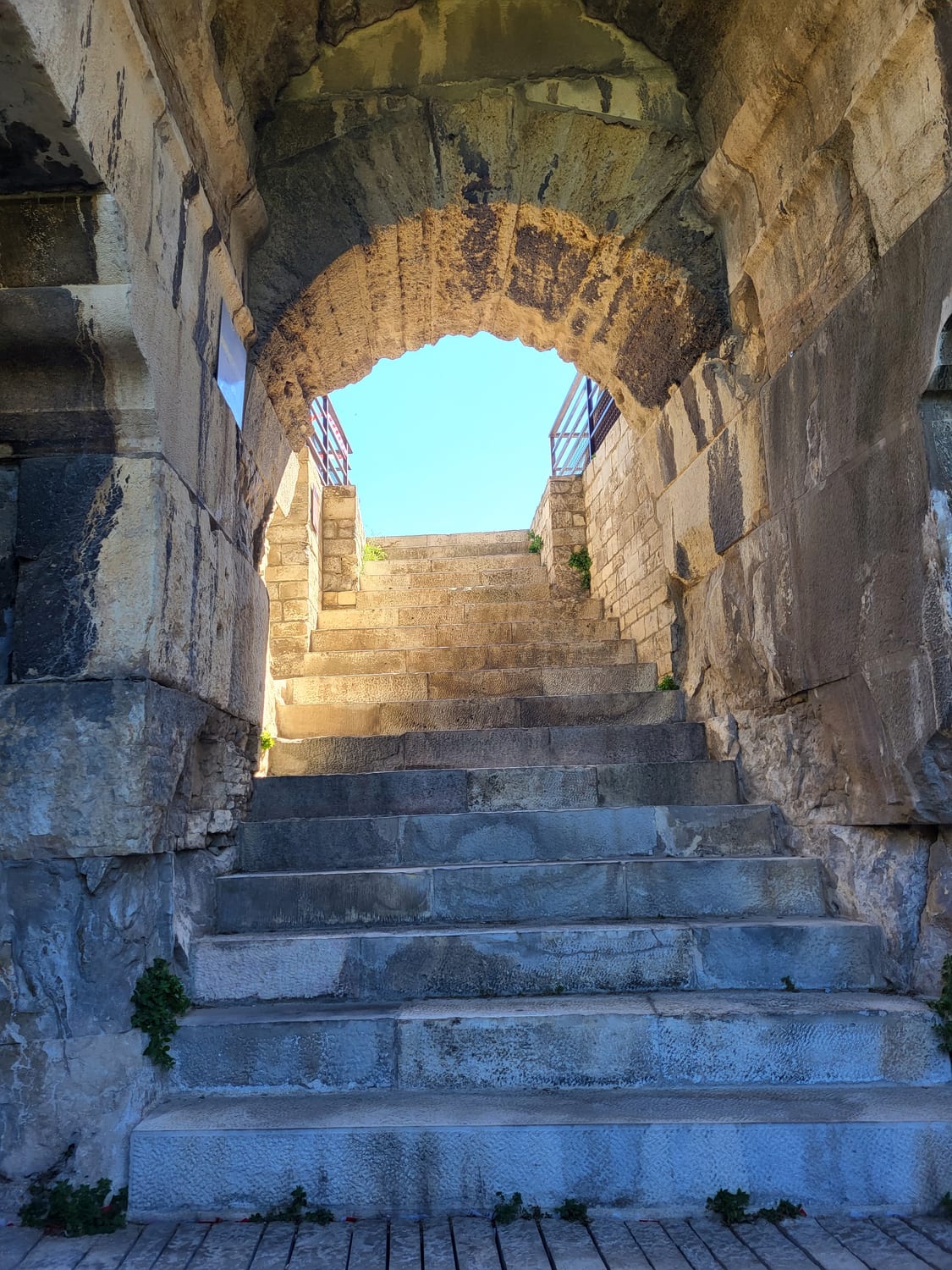 un escalier voûté des Arènes de Nîmes montant vers le ciel à travers l’arc d’un vomitorium