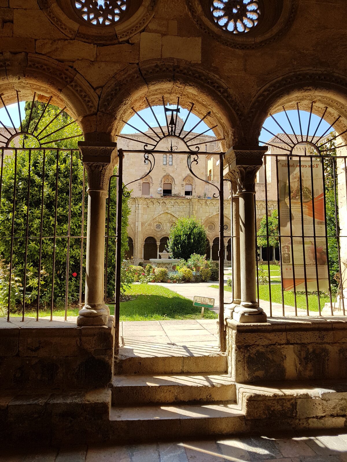 the arcades of the cloister of Tarragona Cathedral seen from the gallery, with the garden beyond the grille