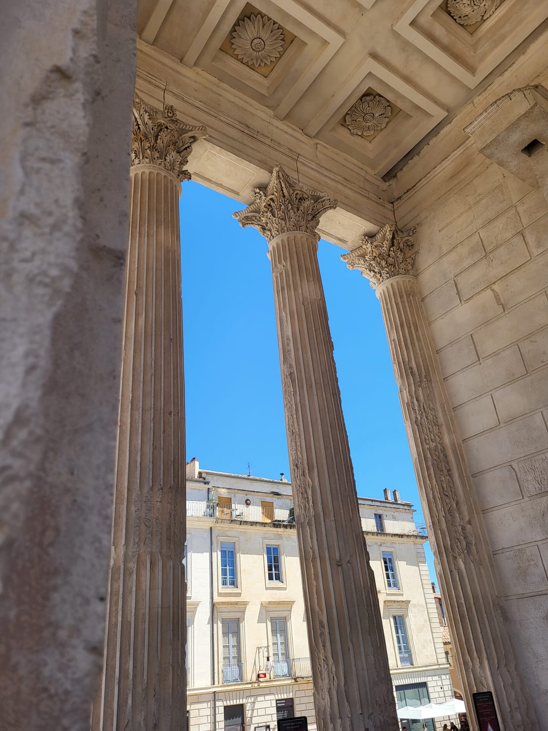 le colonne del portico della Maison Carrée di Nîmes che inquadrano la piazza e la parete di vetro del Carré d’Art