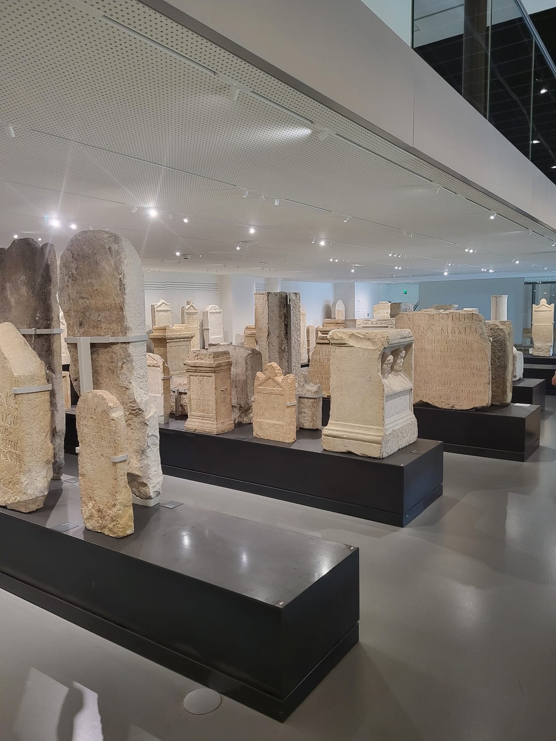 la sala del lapidario al Musée de la Romanité di Nîmes, con stele e iscrizioni funerarie romane disposte su basamenti scuri