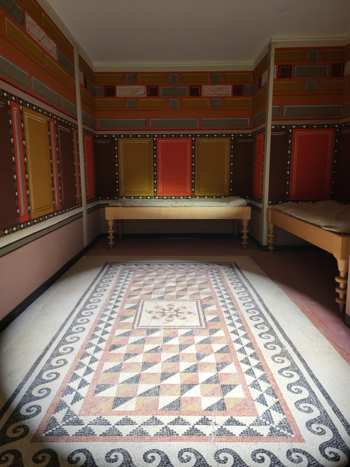 la ricostruzione di una stanza romana al Musée de la Romanité di Nîmes, con le pareti dipinte a pannelli rossi e gialli e il pavimento a mosaico