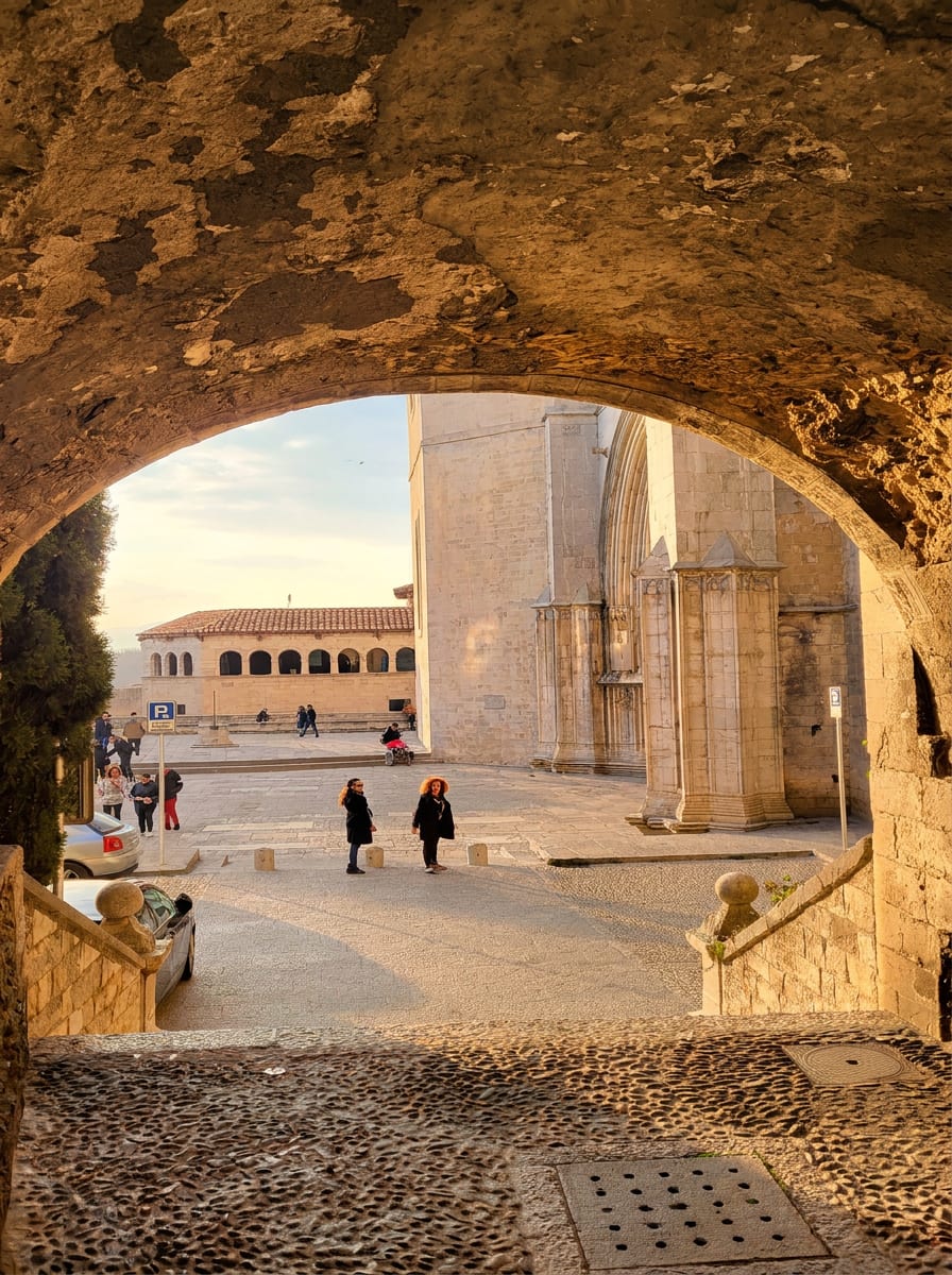 l’arco del Portal de Sobreportes a Girona che inquadra la piazza della cattedrale con i passanti in controluce